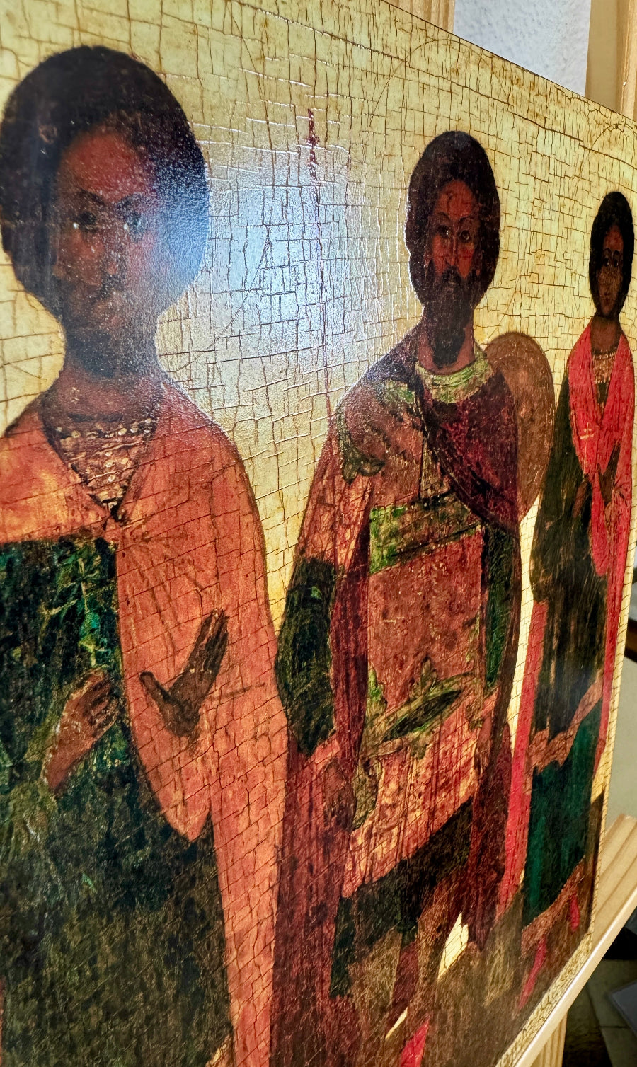 A close-up of a cracked, vintage-style painting depicting three figures in robes against a textured gold background.