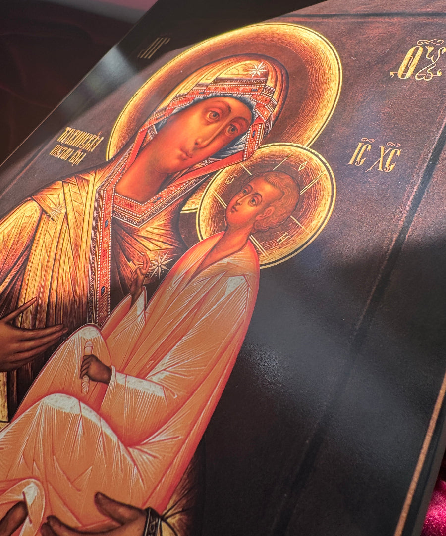 Icon of a religious figure virgin Mary holding a child with gold accents on a dark background