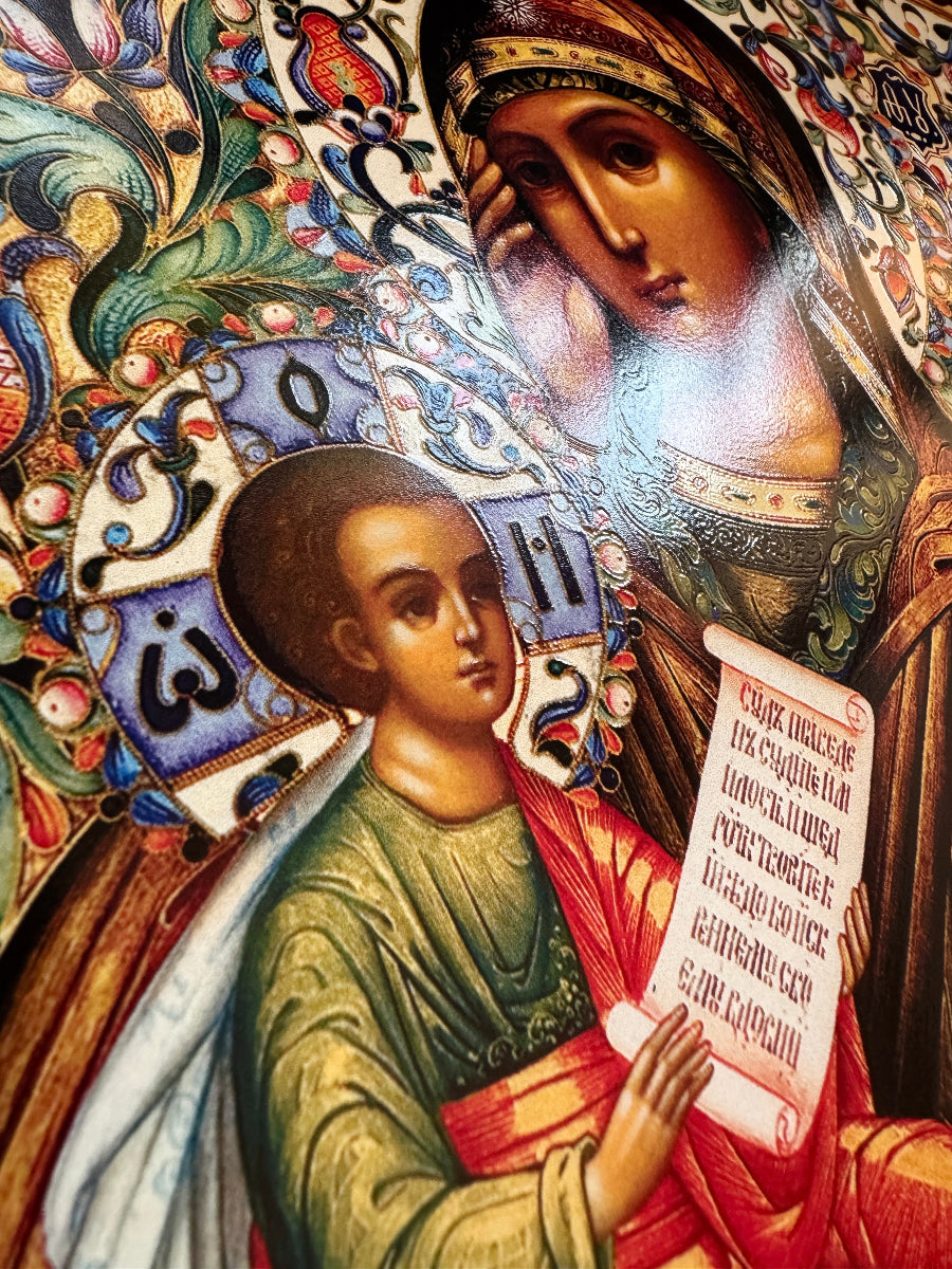 A close-up of a colorful religious icon painting showing two haloed figures, likely the Virgin Mary and Child, with ornate floral and scroll details and a bright glare on the upper right.